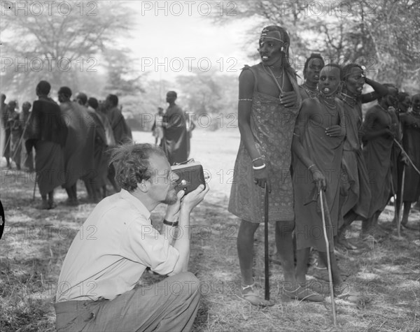 Filming Maasai dancers. A European man identified as 'Johnson' crouches down to take a photograph of a group of male Maasai dancers at the welcoming ceremony provided for Princess Margaret. Amboseli, Tanganyika Territory (Tanzania), 23 October 1956. Amboseli, Kilimanjaro, Tanzania, Eastern Africa, Africa.