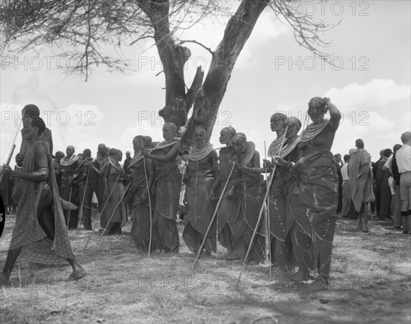 Female Maasai dancers. A group of female Maasai dancers with sticks wait to perfom at a welcoming ceremony being held for Princess Margaret. Naked from the waist up, they wear ornate jewellery including heavily beaded necklaces and earrings. Amboseli, Tanganyika Territory (Tanzania), 23 October 1956. Amboseli, Kilimanjaro, Tanzania, Eastern Africa, Africa.
