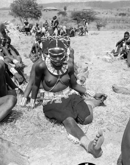 Portrait of a female Wakamba dancer. A semi-naked female Wakamba dancer sits on the ground, leg outstretched. Her ceremonial dress, worn for Princess Margaret's visit, includes an elaborately beaded necklace, headband and belt. Kenya, 22 October 1956. Machakos, East (Kenya), Kenya, Eastern Africa, Africa.