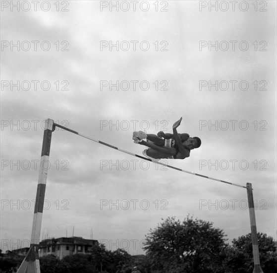Joseph Lenesae jumps the bar. Kenyan high jumper Joseph Lenesae is captured in mid-air as he practices for the 1956 Olympic games. India, 2 November 1956. India, Southern Asia, Asia.