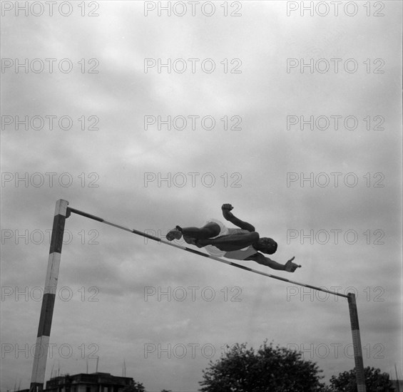 Patrick Etola jumps the bar. Ugandan high jumper Patrick Etola stretches over the high jump pole at a warm-up session for the 1956 Olympic games. India, 2 November 1956. India, Southern Asia, Asia.