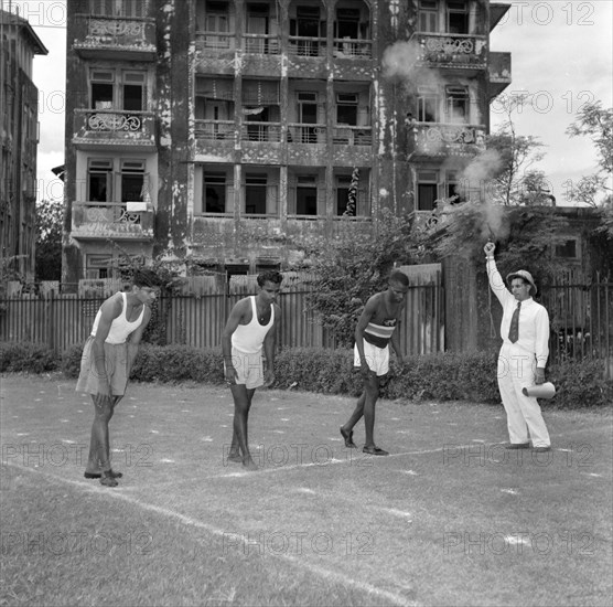 On the starting blocks. A starting pistol fires for three Olympic athletes on the starting line of a practice race. India, 2 November 1956. India, Southern Asia, Asia.