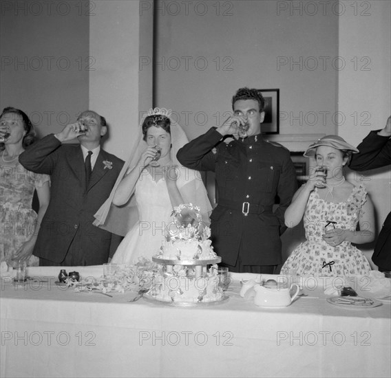 Toasting absent friends. The newlywed Jones and Buckley couple and their family drink a toast to absent friends at their wedding reception. Kenya, 8 December 1956. Kenya, Eastern Africa, Africa.