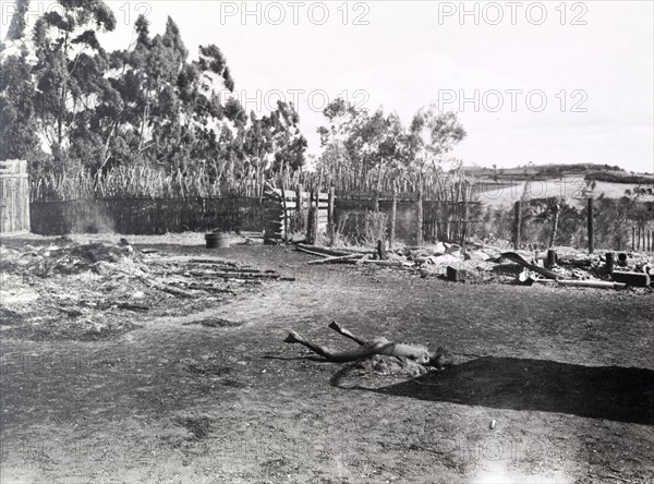 Child murdered by Mau Mau. The body of a murdered child lies rigid in the smoking ruins of a village, victim of a raid by Mau Mau fighters. Kenya, circa 1953. Kenya, Eastern Africa, Africa.