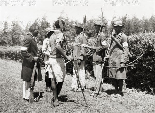 Kikuyu Home Guards. An official photograph of six Kikuyu Home Guards, armed with spears and bows and arrows. One man carries a rifle. Nyeri, Kenya, 1952. Nyeri, Central (Kenya), Kenya, Eastern Africa, Africa.