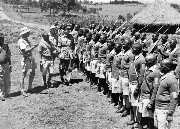 Inspecting the Home Guard at Kangare. An official photograph of Colonel Morcombe, director of the Kikuyu Home Guard, inspecting a unit of the guard in their new uniforms. They appear to be doing drill with sticks rather than rifles. Kangare, Kenya, 1953. Kangare, Central (Kenya), Kenya, Eastern Africa, Africa.