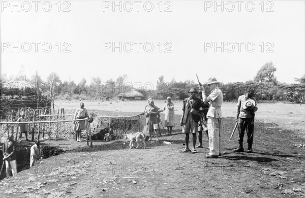 Home Guards at a Kikuyu security village. Armed Kikuyu Home Guards wait for a European man to load his rifle at a fortified security village. To the left, Kikuyu men can be seen digging a moat to provide further protection against Mau Mau attack. Kenya, circa 1955. Kenya, Eastern Africa, Africa.