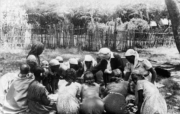 Nellie Grant teaches Kikuyu women. Nellie Grant, the wife of settler farmer Jos Grant and mother of Elspeth Huxley (nee Grant), teaches a domestic science class outdoors for the wives of Kikuyu farmers. Kenya, circa 1955. Kenya, Eastern Africa, Africa.