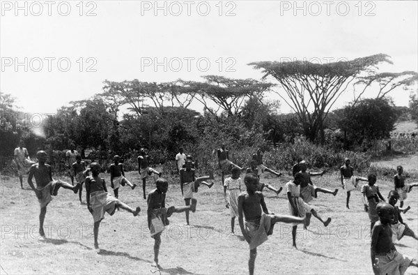 Kikuyu children exercising. Children perform coordinated exercises in a secure village established for the families of the Kikuyu Home Guard. Kenya, circa 1953. Kenya, Eastern Africa, Africa.