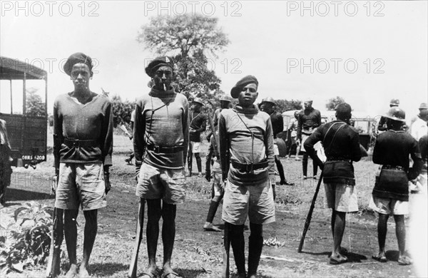 Three Home Guards. Three Kikuyu Home Guards stand to attention for their photograph, wearing uniforms and carrying mock rifles made of wood. Kenya, circa 1953. Kenya, Eastern Africa, Africa.