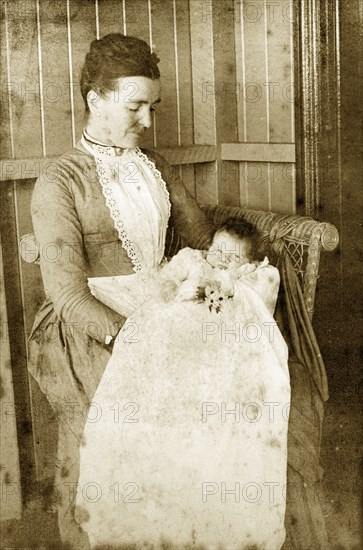 Mrs Robertson and Molly Harr'. A woman identified as 'Mrs Robertson' looks down at 'Molly Harr', a baby who sits on her knee wrapped in a white gown. Queensland, Australia, 5 August 1890., Queensland, Australia, Australia, Oceania.