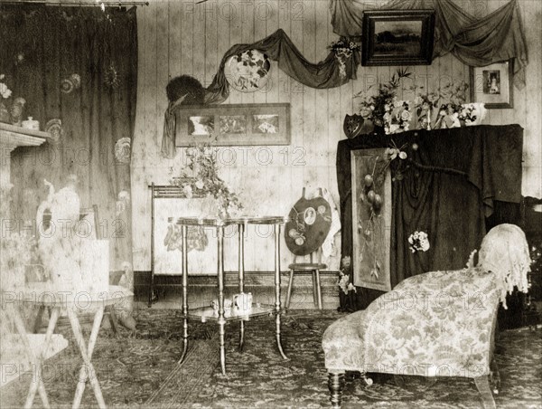 The drawing room at 'Nundora'. A typical Victorian drawing room at 'Nundora', the Brodribb family's house. Furnished with a heavily patterned rug and armchair, the room's surfaces and walls are busily decorated with pictures and ornaments. Toowoomba, Australia, circa 1890. Toowoomba, Queensland, Australia, Australia, Oceania.