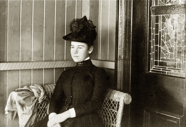 Laura Hart' on the veranda. Portrait of a Victorian lady identified as 'Laura Hart'. Dressed in a dark pinstripe dress and a hat decorated with dark flowers, she sits in a wickerwork chair on the veranda of a colonial house. Queensland, Australia, circa 1895., Queensland, Australia, Australia, Oceania.