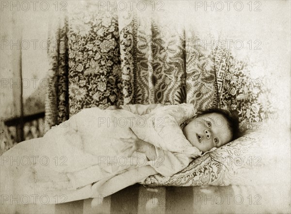 Portrait of a baby, Australia. A young baby dressed in a white gown gazes curiously into the distance against a backdrop of patterned cloth. Queensland, Australia, circa 1895., Queensland, Australia, Australia, Oceania.