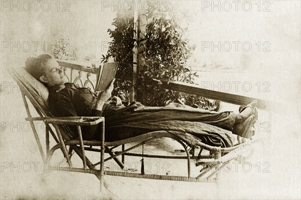Relaxing on the veranda. Ellen May Pughe relaxes in a wicker chaise longue as she reads from a book on the veranda of a house. Near Brisbane, Australia, circa 1895., Queensland, Australia, Australia, Oceania.