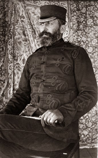 Victorian man in uniform, Australia. Portrait of a Victorian man dressed in a dark, military-style uniform. He wears a flat-peaked cap with leather gloves and holds a cane across his knee. Queensland, Australia, circa 1895., Queensland, Australia, Australia, Oceania.