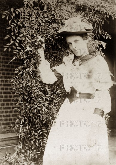 Portrait of a Victorian lady, Australia. A Victorian lady strikes a pose beside a trellis covered in creepers. She wears a white dress teamed with a wide belt and floral hat. Queensland, Australia, circa 1895., Queensland, Australia, Australia, Oceania.