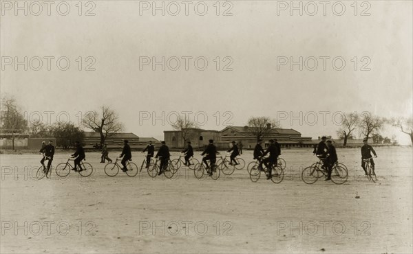 Musical bicycle ride. Identified as 'The 1st Buffs' bicycle section', a group of British cyclists dressed in dark sports uniforms ride around an open space in circles. According to the original caption, this is a 'musical ride'. India, circa 1895. India, Southern Asia, Asia.