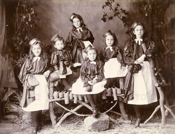 Portrait of girls in uniform, Murree. A family of girls pose for the camera wearing distinctive pinafore uniforms with hats pinned to the sides of their heads. Murree, Punjab, India (Punjab, Pakistan), circa 1895. Murree, Punjab, Pakistan, Southern Asia, Asia.