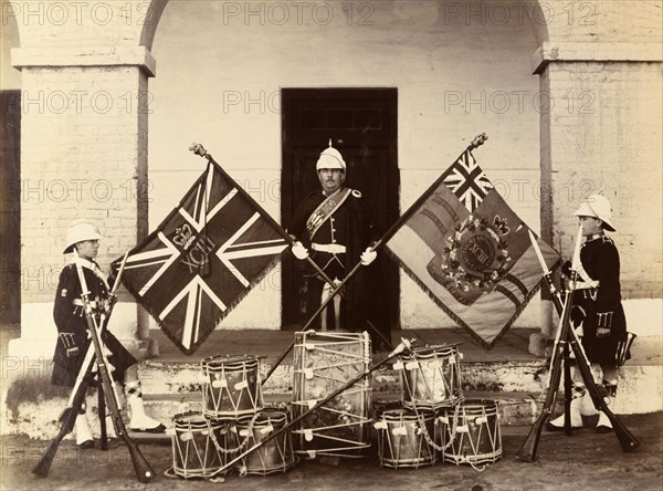Colours of the 93rd Highlanders. Three uniformed soldiers from the 93rd Highlanders pose proudly with 
the colours of their regiment beside a display of crossed bayonets and military drums. India, circa 1895. India, Southern Asia, Asia.