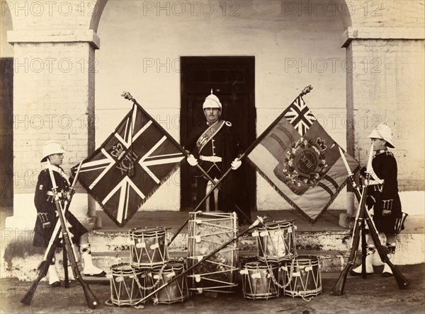 Colours of the 93rd Highlanders. Three uniformed soldiers from the 93rd Highlanders pose proudly with
the colours of their regiment beside a display of crossed bayonets and military drums. India, circa 1895. India, Southern Asia, Asia.