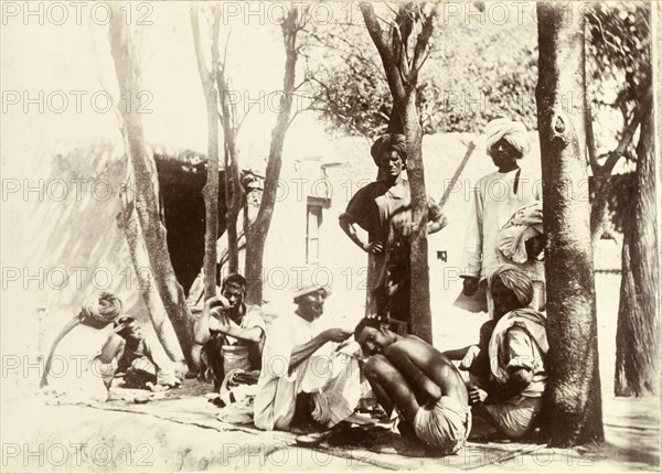 Indian street barbers. Turbaned Indian men sit on rugs in the street, providing a barber service for local men and boys. India, circa 1895. India, Southern Asia, Asia.