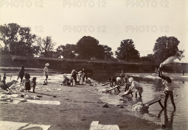 Washing day at the river. Washing clothes at the edge of a river. Several Indian men thrash and scrub fabric onto washboards propped up in the water, whilst wet garments are spread out to dry on the riverbank. India, circa 1895. India, Southern Asia, Asia.