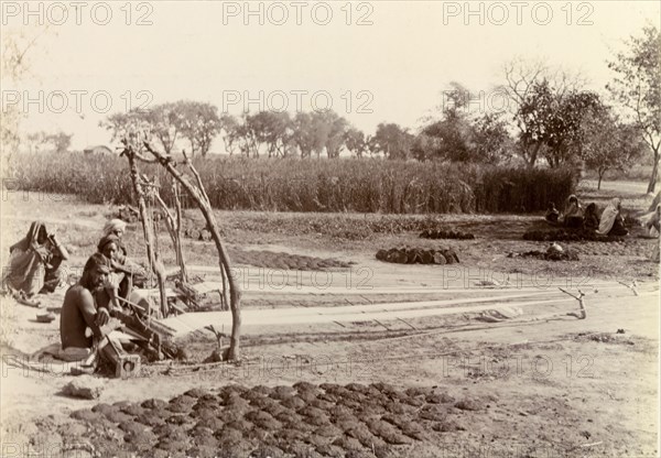 Weaving in the fields. Indian weavers pause for a moment, crouched beside their hand looms. The long lengths of fabric they are working on can be seen stretched out on stakes in the ground. India, circa 1895. India, Southern Asia, Asia.