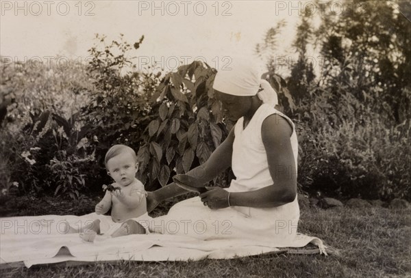 Gwynneth at seven months. An African ayah (nursemaid) identified as 'Salima' supports a seven month old baby, Gwynneth Wallhouse, as she plays on a rug in the garden. Tanganyika Territory (Tanzania), circa 1930. Tanzania, Eastern Africa, Africa.