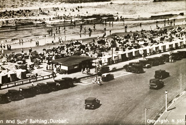 The seafront at Durban. Motorcars line the seafront at Durban. Crowds of people with parasols pack the beach to sunbathe whilst others swim in the sea. Durban, Natal (KwaZulu Natal), South Africa, circa 1936. Durban, KwaZulu Natal, South Africa, Southern Africa, Africa.
