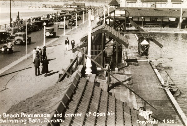 The beach promenade at Durban. Groups of people stroll along the beach promenade in Durban beside an open air swimming pool near the seafront. Durban, Natal (KwaZulu Natal), South Africa, circa 1936. Durban, KwaZulu Natal, South Africa, Southern Africa, Africa.