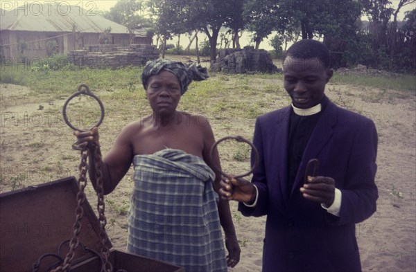 Slave chains at Badagry. A Nigerian woman and priest display metal chains that would once have been fitted around the necks of slaves. These are family heirlooms, brought back from Freetown in Sierra Leone by liberated slaves. Badagry, Nigeria, circa 1970. Badagry, Lagos, Nigeria, Western Africa, Africa.