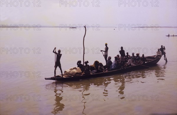 Niger scene. A wooden canoe laden with passengers is steered across the muddy waters of the River Niger. Nigeria, 1965. Nigeria, Western Africa, Africa.