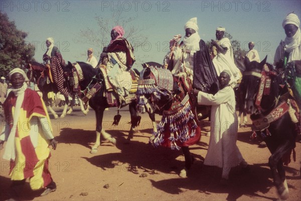 Decorated horses, Nigeria. Men dressed in ceremonial attire ride horses decorated with tassles and ornate bridles at a procession marking the end of Ramadan. Zaria, Nigeria, 1958. Zaria, Kaduna, Nigeria, Western Africa, Africa.