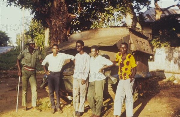 Damaged tank in Onitsha. Five young men pose for the camera, leaning against an armoured tank that has been damaged during the Nigerian Civil War (1967-70). One is a soldier, the others are college students and students from the Dennis Memorial Grammar School. Onitsha, Nigeria, circa 1970. Onitsha, Anambra, Nigeria, Western Africa, Africa.