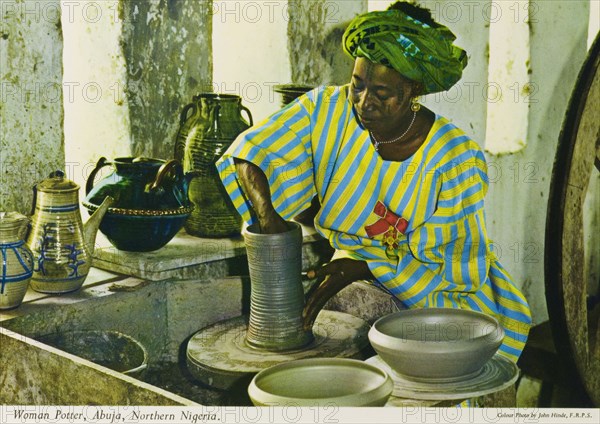 Potter's studio, Nigeria. A colourful tourist postcard depicts a Nigerian craftswoman working on a clay vase at a potter's wheel. A selection of finished, glazed pots sits on the windowsill of her studio. Abuja, Nigeria, circa 1975. Abuja, Abuja, Nigeria, Western Africa, Africa.