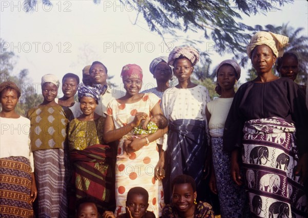 Midwife Olayinka with maternity patients. A qualified midwife identified as 'Olayinka', stands amongst a group of colourfully dressed women holding a baby. The women surrounding her are all maternity patients at a Church of Nigeria hospital. Ijan, Nigeria, circa 1963. Ijan, Kwara, Nigeria, Western Africa, Africa.