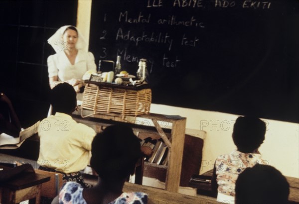 PTS nursing exam. A qualified nurse presides over a Preliminary Training School (PTS) entrance exam, held for nurses training to work at a Church of Nigeria hospital. Notes on the blackboard list three parts of the exam, which include a mental arithmetic test, an adaptability test and a memory test. Nigeria, circa 1963. Nigeria, Western Africa, Africa.