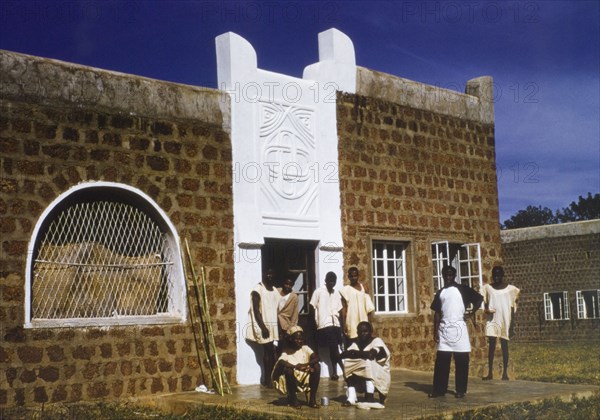 Male patients at a Church of Nigeria hospital. A group of male patients at a Church of Nigeria hospital, loiter outside the entrance to the children's ward. Several wear loosely fitting hospital tunics. Nigeria, circa 1970. Nigeria, Western Africa, Africa.