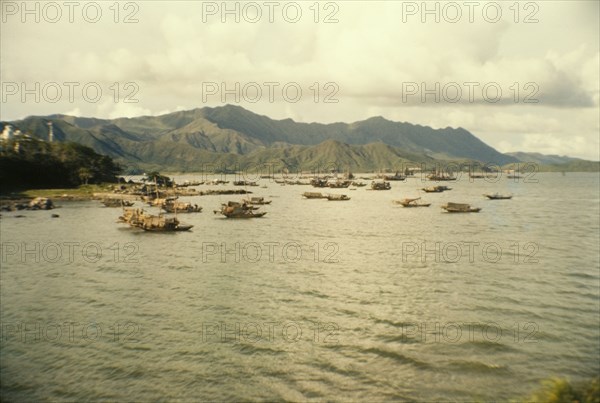 Fishing boats off Tai Po. Mountains form a backdrop to a fleet of Chinese sampans that bob up and down off the coast of Tai Po. Tai Po, Hong Kong, People's Republic of China, July 1960. Tai Po, Hong Kong, China, People's Republic of, Eastern Asia, Asia.