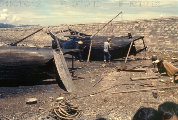 Re-caulking a sampan. Fishermen re-caulk the upturned bottoms of their sampans, filling in the cracks caused by weathering to ensure their vessels are waterproof. Tai Po, Hong Kong, People's Republic of China, August 1960. Tai Po, Hong Kong, China, People's Republic of, Eastern Asia, Asia.