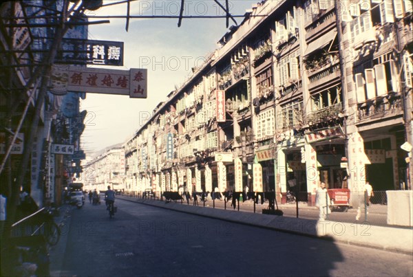 A street in Wan Chai. A row of tall shop buildings, littered with signs written in Chinese script, line a city street. Wan Chai, Hong Kong, People's Republic of China, July 1960. Wan Chai, Hong Kong, China, People's Republic of, Eastern Asia, Asia.