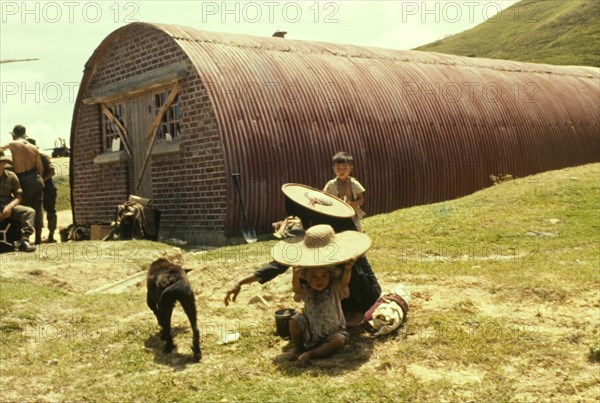 Container shed at Hebe Hill. A family sits on the ground outside a tubular-shaped container shed, constructed from bricks and corrugated iron, at Hebe Hill. Hong Kong, People's Republic of China, July 1960., Hong Kong, China, People's Republic of, Eastern Asia, Asia.