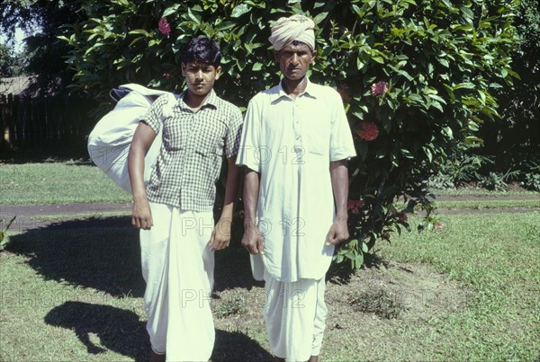 A 'dhobi' and his assistant. Outdoors portrait of a 'dhobi' (laundryman) and his assistant carrying laundry at the Mancotta tea estate. Dibrugarh, Assam, India, 1960. Dibrugarh, Assam, India, Southern Asia, Asia.
