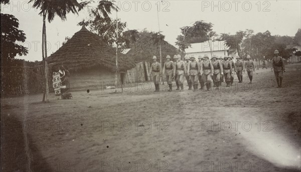 European soldiers in East Africa. A group of uniformed European soldiers wearing solatopis march in line through a village. Tanzania, 1906., Eastern Africa, Africa.
