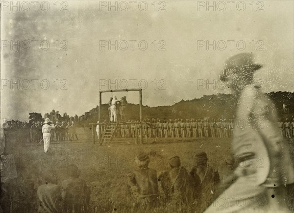 Colonial execution. An executioner prepares for two African men to be hung from a wooden scaffold, their execution to be witnessed by colonial troops and officers. German East Africa (Tanzania), 1906. Tanzania, Eastern Africa, Africa.
