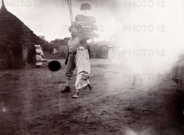 Woman escorted to execution. An African woman is escorted across a compound by an African soldier or guard, her hands apparently tied or chained behind her back. A caption indicates she is being led to execution. German East Africa (Tanzania), 1906. Tanzania, Eastern Africa, Africa.