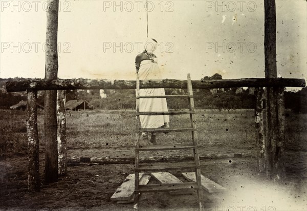 Colonial execution of a woman. The body of an African woman hangs by the neck from a wooden scaffold, her head wrapped in a large blindfold. German East Africa (Tanzania), 1906. Tanzania, Eastern Africa, Africa.