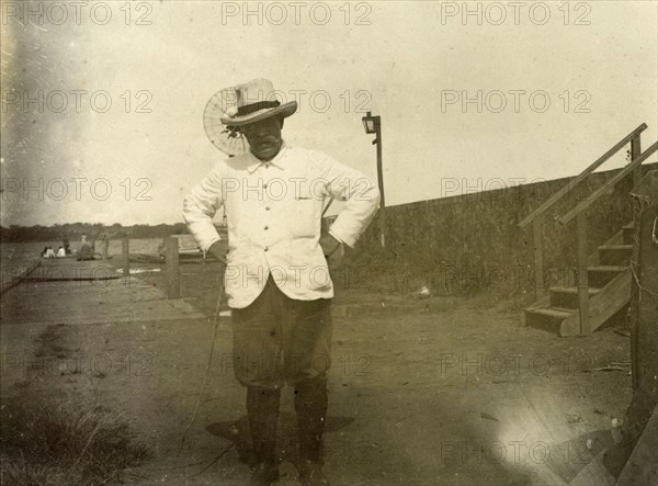 District Commisioner of Entebbe. Portrait of a colonial officer identified as 'James Martin', the District Comissioner of Entebbe, Uganda. He stands, hands on hips, near a jetty on the banks of a river or lake. German East Africa (Tanzania), 1906. Tanzania, Eastern Africa, Africa.
