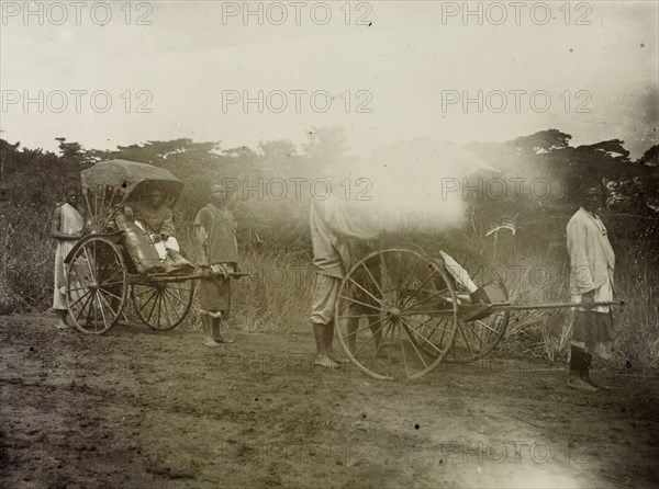 Rickshaw pullers in Uganda. African servants pull rickshaws along a muddy track. Frederick Stanbury (the creator) originally captioned this image 'How I travelled'. Uganda, 1906. Uganda, Eastern Africa, Africa.